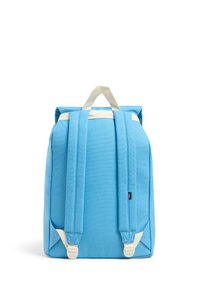 Mochila de lona azul con acentos blancos, forma rectangular, asa superior y correas ajustables. Presenta una etiqueta de marca en el lateral.