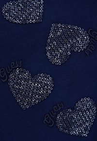 Un tessuto blu navy presenta cinque cuori testurizzati decorati con brillanti strass e la parola "Guess" ricamata in un colore contrastante.