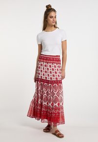 Maxi-Rock in rot-weißen Blumenmustern mit gerafftem Saum, kombiniert mit einem schlichten weißen T-Shirt mit kurzen Ärmeln und braunen Sandalen.