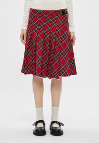 Jupe écossaise rouge avec des plis, comportant des accents verts et noirs. Inclut un détail de boucle noire à la taille. Texture du tissu lisse.