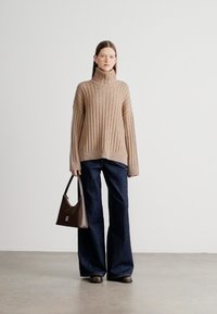 Μπεζ ριγέ πουλόβερ με ζιβάγκο συνδυασμένο με σκούρο μπλε τζιν παντελόνι με φαρδιά πόδια. Το μοντέλο κρατά καφέ τσάντα. Ομαλή υφή, άνετη εφαρμογή και καθαρές γραμμές.