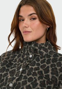 Jasje met luipaardprint in bruin en zwart, gemaakt van vachtachtig materiaal, met zilveren knopen, een hoge kraag en een borstzakdetail.