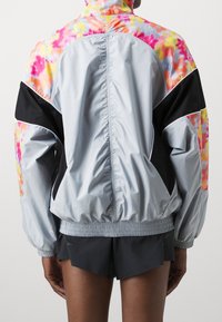 Cortavientos ligero y multicolor con un patrón de tie-dye en rosa, amarillo y naranja, con detalles en negro y dobladillo elástico.