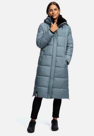 Padded long coat in light blue, featuring a black fur-lined hood, front zip, and snap closures. Worn over black pants and sneakers.