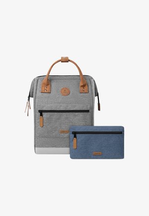 Mochila gris con detalles en cuero marrón y un bolsillo frontal con cremallera. Incluye un estuche azul con cremallera. Ambos presentan una tela texturizada.