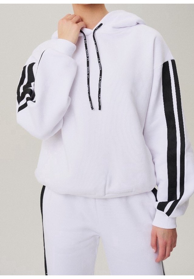 Personne portant un sweat à capuche blanc et un pantalon avec des bandes noires sur les manches et les jambes, tenant un cordon noir près du cou.