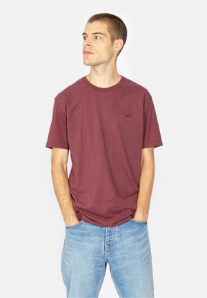Maroon cotton T-shirt with a crew neck, short sleeves, and subtle brand logo in red. Paired with light blue straight-leg jeans.