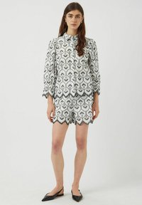 Witte blouse en korte set met zwart bloemenpatroon, gegolfde randen, knoopsluiting aan de voorkant en textuurstof. Zwarte puntige ballerina's.