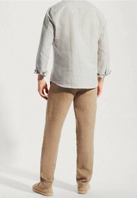 Herrengestreiftes Leinenhemd in Hellgrau und Weiß, kombiniert mit beigen Leinenhosen. Das Hemd hat hochkrempelbare Ärmel und einen abgerundeten Saum.