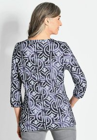Bunte Bluse mit floralem und geometrischem Muster in Lila, Schwarz und Hellblau. Lockere Passform mit Dreiviertelärmeln.