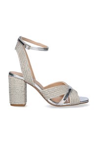 Sandalia de tacón alto plateada con tacón cuadrado y correa en el tobillo. Presenta un material texturizado brillante y tiras frontales entrelazadas.
