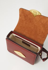 Borsa a mano in pelle rossa con chiusura in metallo dorato, interno in suede e rivestimento beige. Presenta un singolo scomparto e una tracolla.
