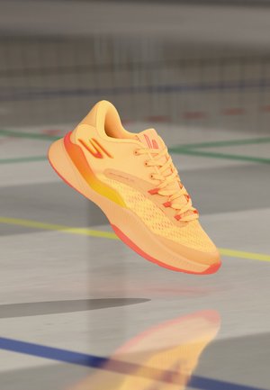 Chaussure de sport orange vif et jaune en suspension au-dessus d'un sol de terrain de sport intérieur avec les lignes du terrain visibles.