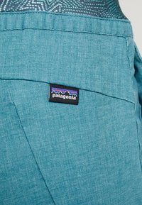 Teal stoffen broekzak met een zwart Patagonia merkembleem dat een berglogo toont en kleurrijke strepen op de tailleband erboven.