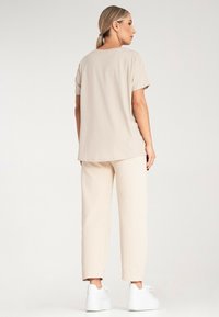 Beżowa bluzka z krótkim rękawem i pasujące szerokie spodnie, wykonane z miękkiego materiału. Białe trampki dopełniają strój. Prosty design, bez wzorów.