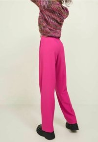 Fuchsiové široké kalhoty s hladkou texturou, ozdobené puky a vysokým pasem, spárované s černými platformovými botami.