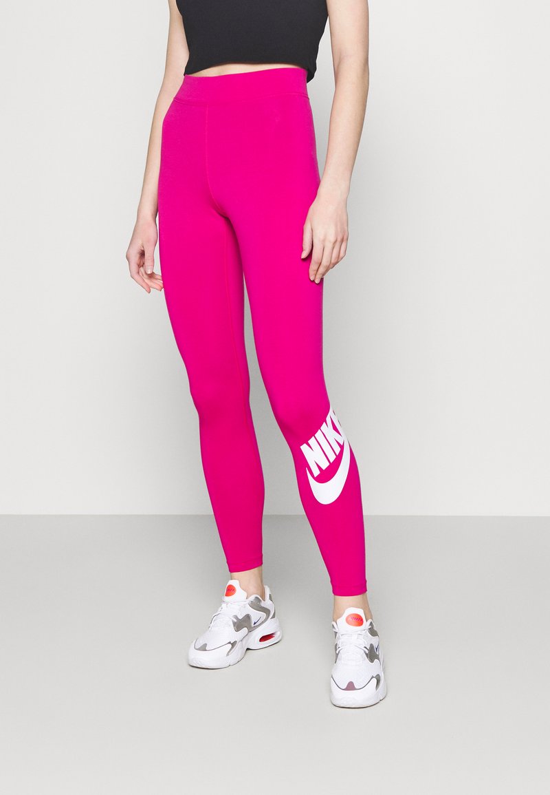 Leggings fucsia con vita alta e grande logo Nike bianco sulla gamba sinistra. Indossati con scarpe da ginnastica bianche e grigie.