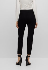 Musta, muotoon laitettu housut sileällä pinnalla ja keski-korkealla vyötäröllä, yhdistettynä mustiin korkokenkiin, joissa on nilkkahihnat.