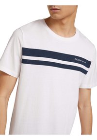 White cotton t-shirt featuring a navy horizontal stripe across the chest, with a logo on the left side and short sleeves.