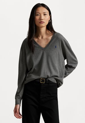 Grau, V-Ausschnitt Pullover aus weichem Stoff mit einem lockeren Schnitt; verfügt über lange Ärmel und ein kleines blaues Logo auf der linken Brust, kombiniert mit schwarzen Hosen.