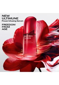 Flacon du sérum dynamisant Shiseido Ultimune centré sur de grands pétales de fleurs rouges avec des traînées de lumière rouge et or dynamiques.