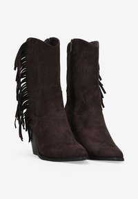 Botas de tobillo de ante marrón con puntera afilada, cierre de cremallera lateral y detalles de borlas a lo largo de los lados exteriores. Tacón cuadrado para mayor altura.