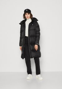 Black puffer coat with hood, zipper, and side pockets. Paired with a white turtleneck, black pants, and white sneakers. Black cap adds detail.