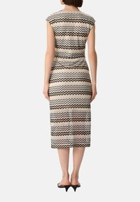 Figurbetontes Midikleid im Zickzackmuster, mit Schwarz, Beige und Cremefarben. Weicher Stoff mit kurzen Ärmeln und taillierter Taille.