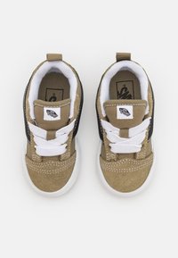 Zapatillas de ante en tonos marrón y negro con cordones blancos y una etiqueta de tela. Presentan una punta redonda, un cuello acolchado y una suela de goma texturizada.