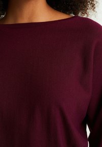 Mörkröd stickad tröja med vid halsringning, mjuk textur och avslappnad passform, med släta sömmar och utan dekorationer.