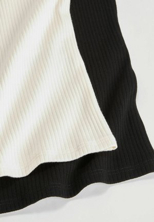 Paita valmistettu ribbikankaasta, jossa on väri-blokki -design, joka sisältää valkoisia ja mustia osia, tekstuuripinta ja kaareva helma.