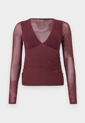 Haut bordeaux à manches longues avec manches en mesh transparent et encolure en V, présentant un détail froncé sur les côtés et un corps en tissu uni.