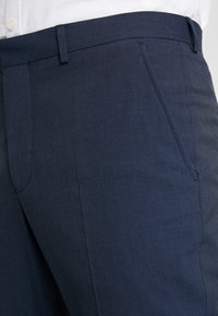 Marineblauwe broek met een geruit patroon, voorzien van zijzakken en een gladde textuur. Getailleerde pasvorm met een verborgen tailleband.