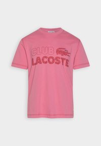 Rosa kortärmad T-shirt med texten "CLUB LACOSTE" och krokodil-logga tryckt i rött över bröstet, rundhalsad krage.