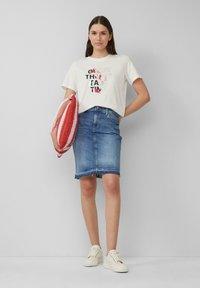 Witte grafische T-shirt met tekst, blauwe denim kokerrok met rafelige zoom, rode en witte gestreepte tas en crèmekleurige sneakers.