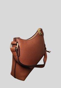 Borsa a tracolla marrone in pelle testurizzata con cerniera dorata e tracolla regolabile su sfondo grigio chiaro.