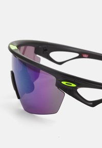 Schwarze Sportsonnenbrille mit einem w-wraparound Design, lila Verlaufsgläsern und grünen Akzenten. Leichtes Gestell mit belüfteten Bügeln.