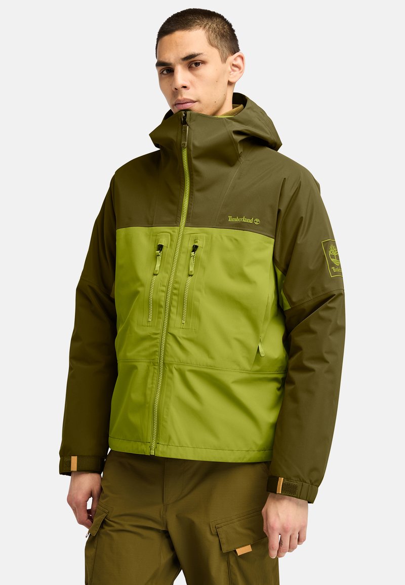Chaqueta color bloqueada en verde y oliva con capucha, que cuenta con dos bolsillos frontales con cremallera, puños ajustables y acentos del logo de Timberland.
