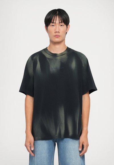 T-shirt noir surdimensionné avec motif tie-dye vert, encolure arrondie et manches courtes. Présente un logo brodé sur la poitrine.