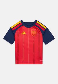 Camisola curta vermelha com riscas verticais, detalhes em azul-marinho, logótipo dourado e cores da bandeira espanhola nos ombros. Feita de material leve e suave.