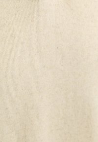 Roomkleurige stof met een zachte, gladde textuur en subtiele, onregelmatige stippen. Het breipatroon is stevig geweven en uniform.