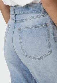 Jasnoniebieskie dżinsy o wysokim stanie, klasycznym designie pięciu kieszeni oraz subtelnym wyblaknięciu. Materiał ma miękkie, teksturowane wykończenie.