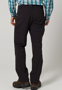 Pantalons noirs d'extérieur en matériau léger, au design fuselé. Les coutures visibles et les détails des poches renforcent la fonctionnalité.