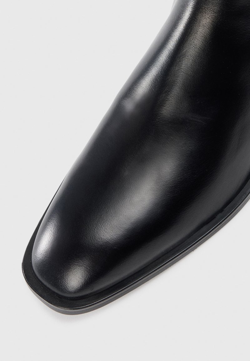 Bottine en cuir noir avec un bout pointu, surface lisse et design minimaliste. Présente une semelle noire robuste et un profil épuré.