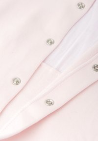 Tela de color rosa claro con broches de metal plateado, que presenta una textura suave y un diseño sencillo, mostrando un borde limpio y cosido.