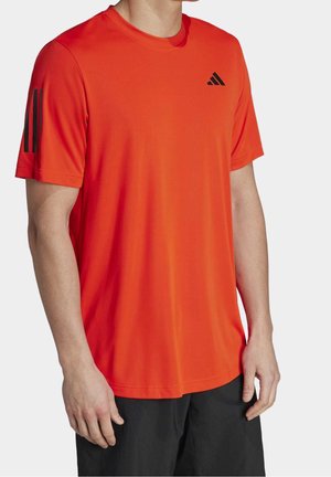 Man draagt een feloranje sport-T-shirt met zwart logo op de borst en zwarte strepen op de linker mouw, gecombineerd met zwarte korte broek.