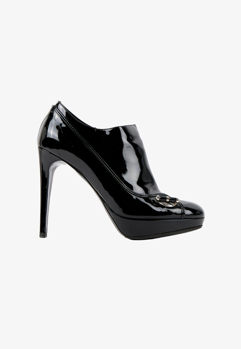 Chaussure à talons hauts noire brillante avec semelle compensée et boucle métallique décorative sur le dessus, vue de profil.
