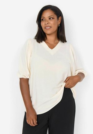 Light cream, V-neck blouse with balloon sleeves and gathered cuffs, paired with black pants. Smooth texture, relaxed fit, minimal design.