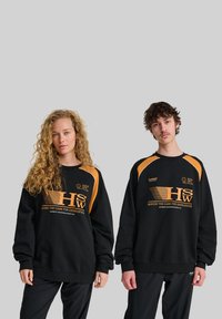 Svarta oversized hoodie med oranga accenter, prydda med grafisk tryck och logotyp. Strukturerad tyg med elastiska muddor, stylad med svarta byxor.