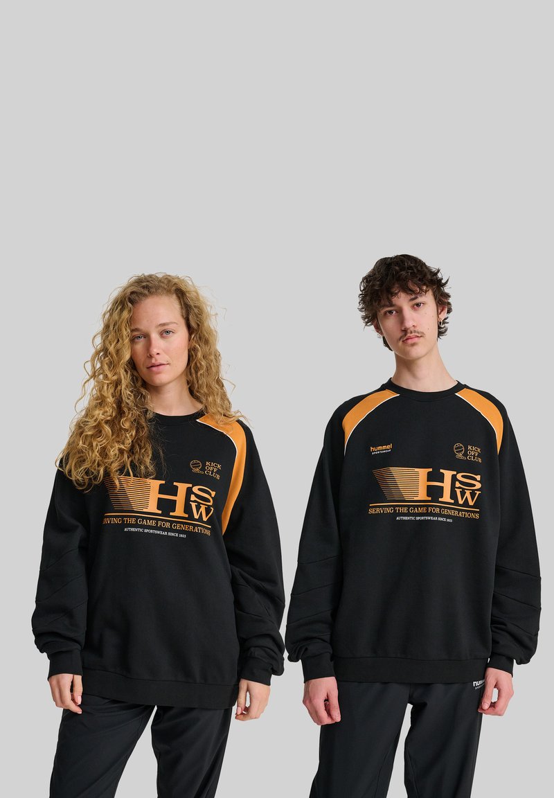 Svarta oversized hoodie med oranga accenter, prydda med grafisk tryck och logotyp. Strukturerad tyg med elastiska muddor, stylad med svarta byxor.